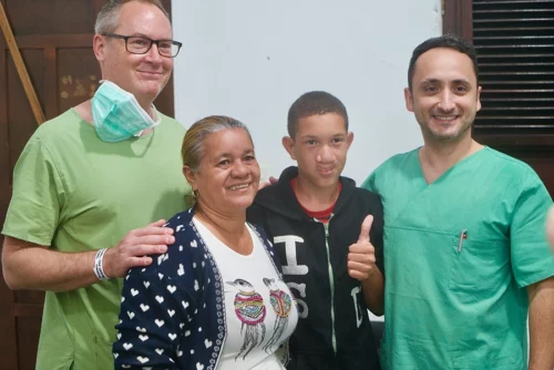Gruppenfoto mit Dr med. Stefan Hessenberger zusammen mit einem erfolgreich operierten Teenager, Angehöriger und einem weiteren Arzt. Der Teenager zeigt glücklich den Daumen hoch.