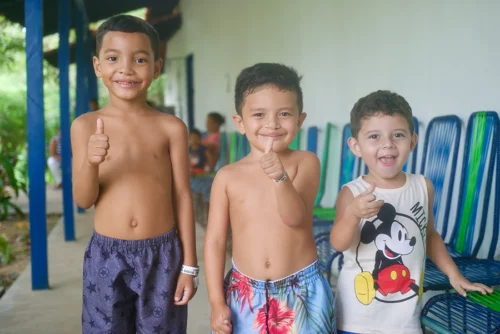Drei Kinder im Wartebereich zeigen lächelnd den Daumen hoch; die zwei linken Kinder sind nach einer Operation wegen Lippen-Kiefer-Gaumen-Spalte.